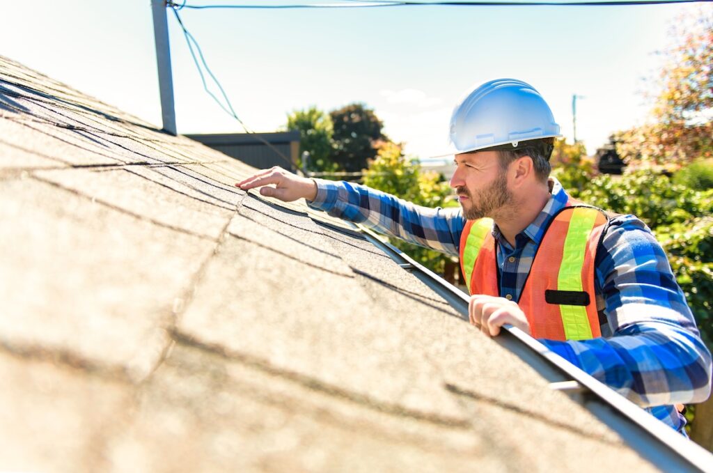 A man with hard hat standing on steps inspecting house roof