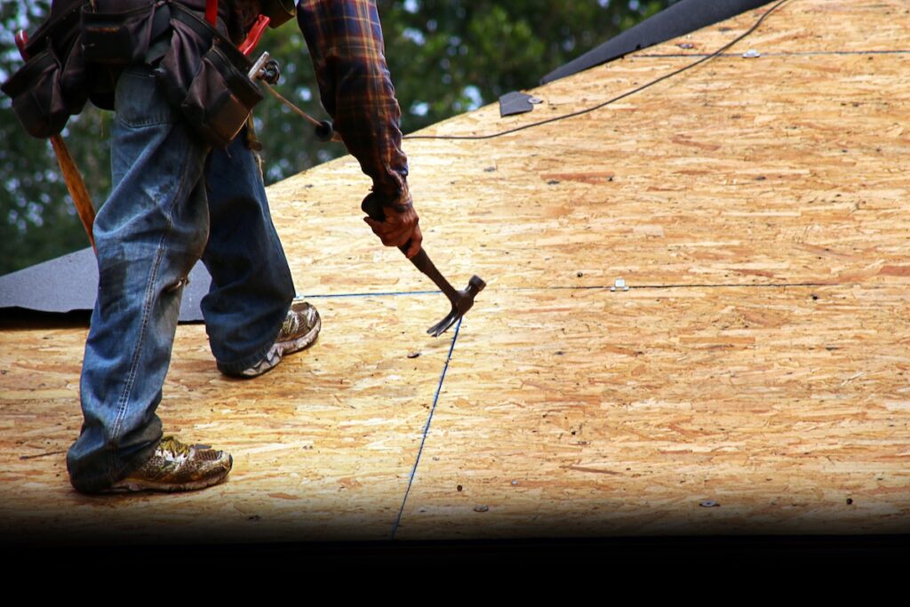 Worker using Nail Puller to remove excess nails on bare rooftop sheathing prior to new felt installation.