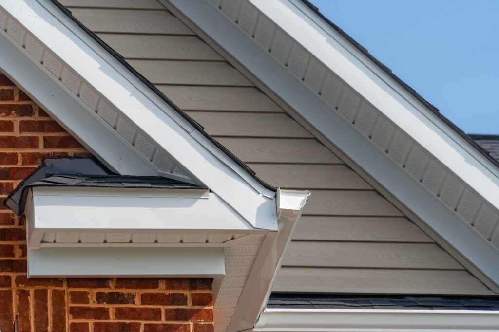 Gable with brick and vinyl siding, white frame gutter guard system, fascia, drip edge, soffit, on a pitched roof attic at a luxury American single family home neighborhood USA