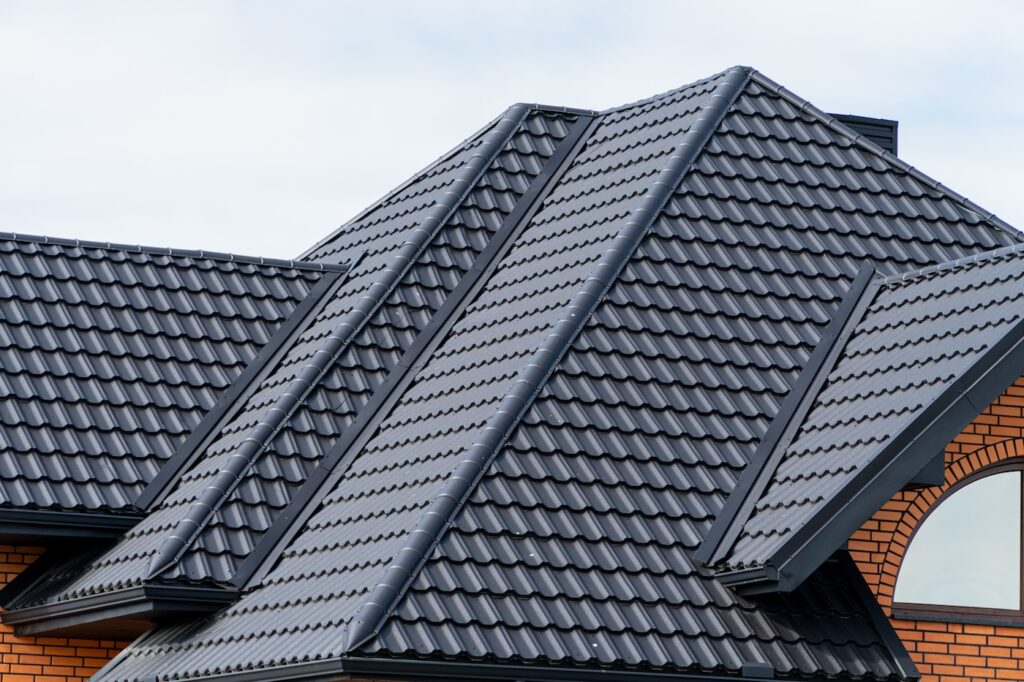 Dark grey metal roof tiles on a modern house. New residential building exterior with brick wall and light sky.