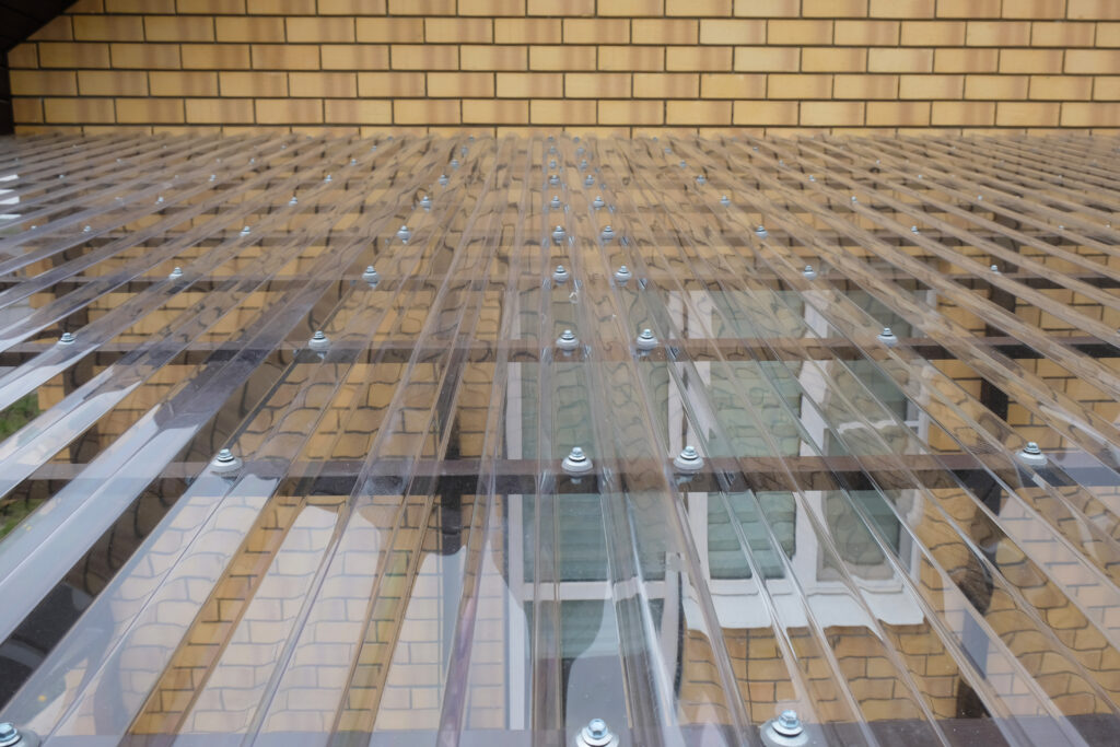 corrugated plastic roof panels Fragment of transparent roof made of profiled polycarbonate with fastening elements in form of thermal washers and self-tapping screws, canopy made of metal structure for terrace of country house, close-up