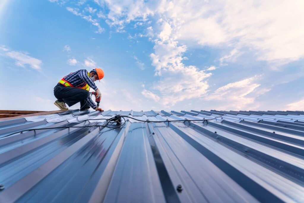 standing seam vs exposed fastener guy standing on top of metallic roof to adjust screws